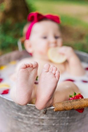 Close-up of tiny feet in milk bath with floating fruit and cinnamon sticks.