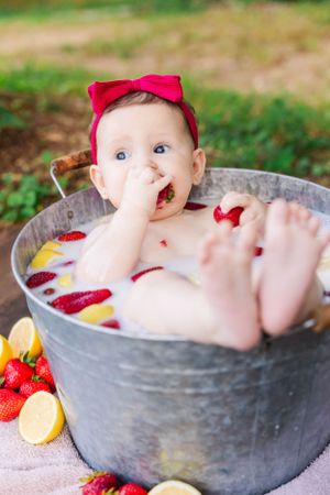 Sweet bath photography setup with fruit and milk in rustic metal tub outdoors.
