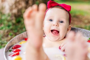 Joyful bath time portrait with floating fruits and red bow accessory.