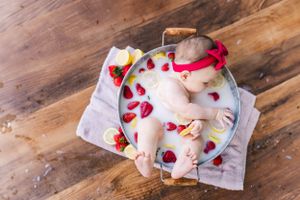 A milk bath photography setup with rose petals and red accents on a wooden floor.