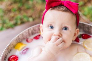 Baby in a milk bath photography session with red bow and flower petals.