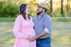 Couple in pink dress and western wear embrace in sunlit outdoor setting.