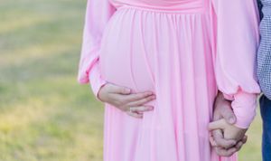 Maternity photos of couple in pink dress and western wear holding baby bump in outdoor setting.
