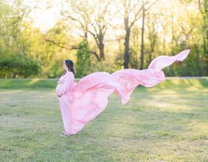 Pink dress flowing dramatically in the breeze during outdoor maternity photoshoot.