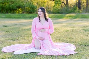 Expectant mother in pink gown sitting on grass during outdoor maternity session.