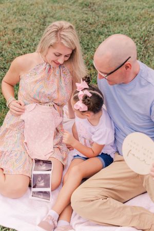 A family sits on a blanket outdoors looking at ultrasound photos together.