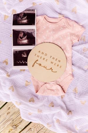 Baby announcement featuring ultrasound images and pink onesie with gold text saying 'And then there were four'.