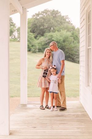 A sweet family moment captured on a white porch with rolling hills in the background.