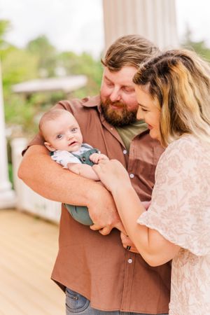 Tender family moment shared between three people on sunny porch with white columns.