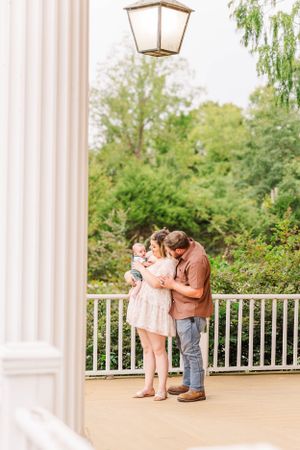 Family members embrace on an elegant white columned porch during photo session.
