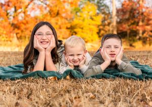 Family members lying on blanket outdoors during autumn photo session.