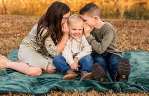 Three people sharing intimate moment on blanket during outdoor photo session.