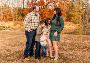 Family of four posing together in an autumn field with golden foliage in background.
