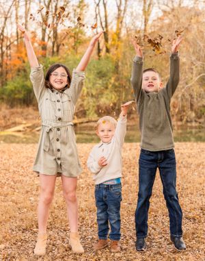 Three people jumping with raised arms against autumn trees background.
