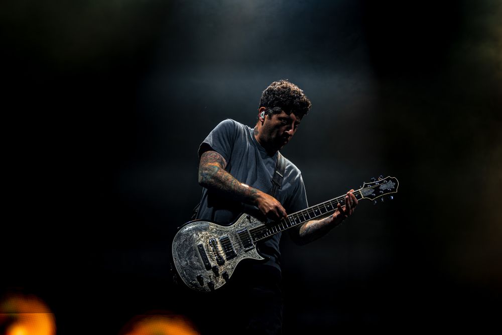 Guitar player performs on stage against dark background with dramatic lighting.