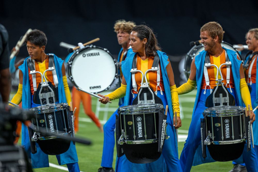 Drummers in bright uniforms perform with marching snare drums at an outdoor event.