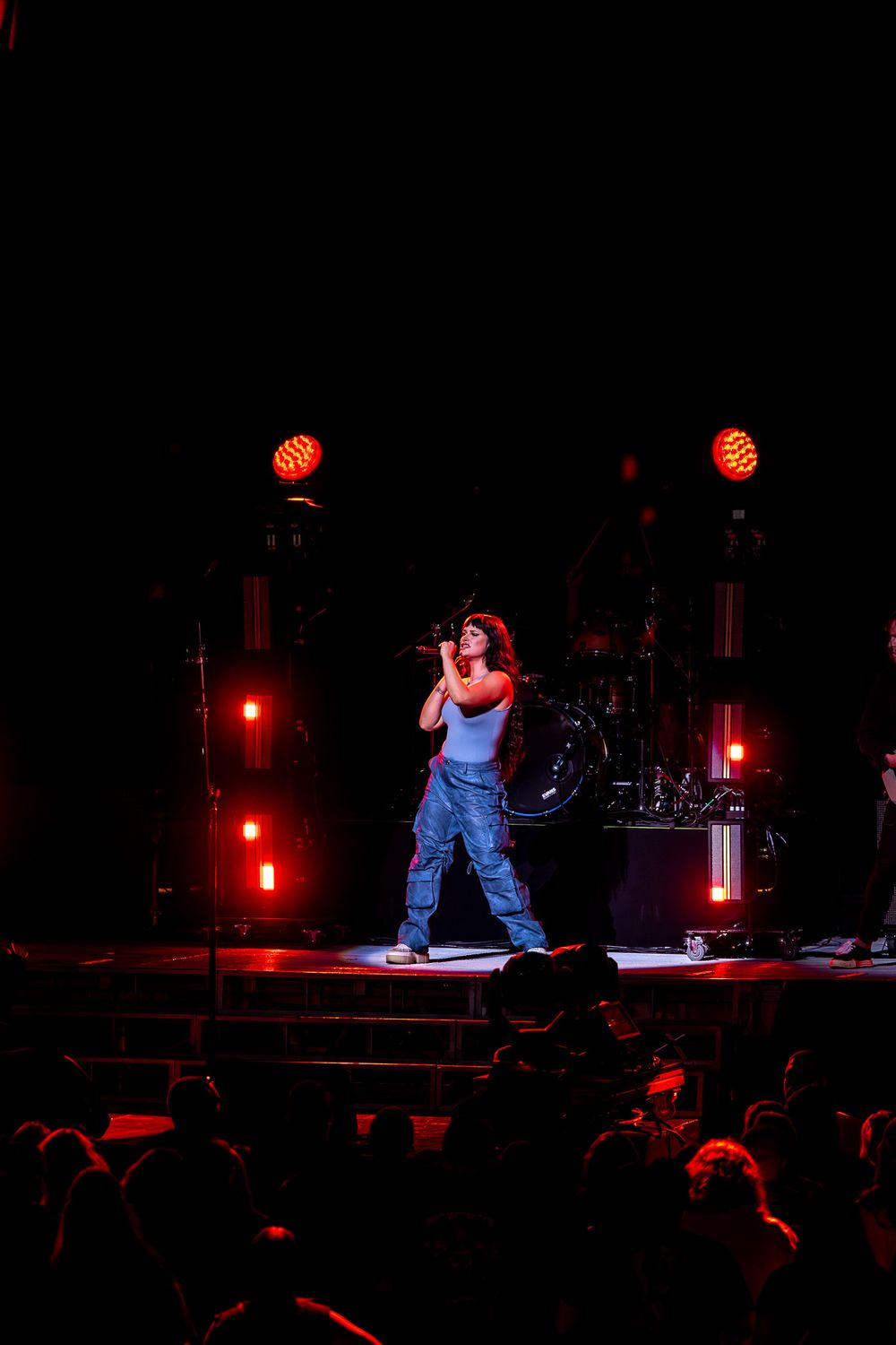 Performer in baggy jeans sings on dark stage with red spotlights illuminating the scene.