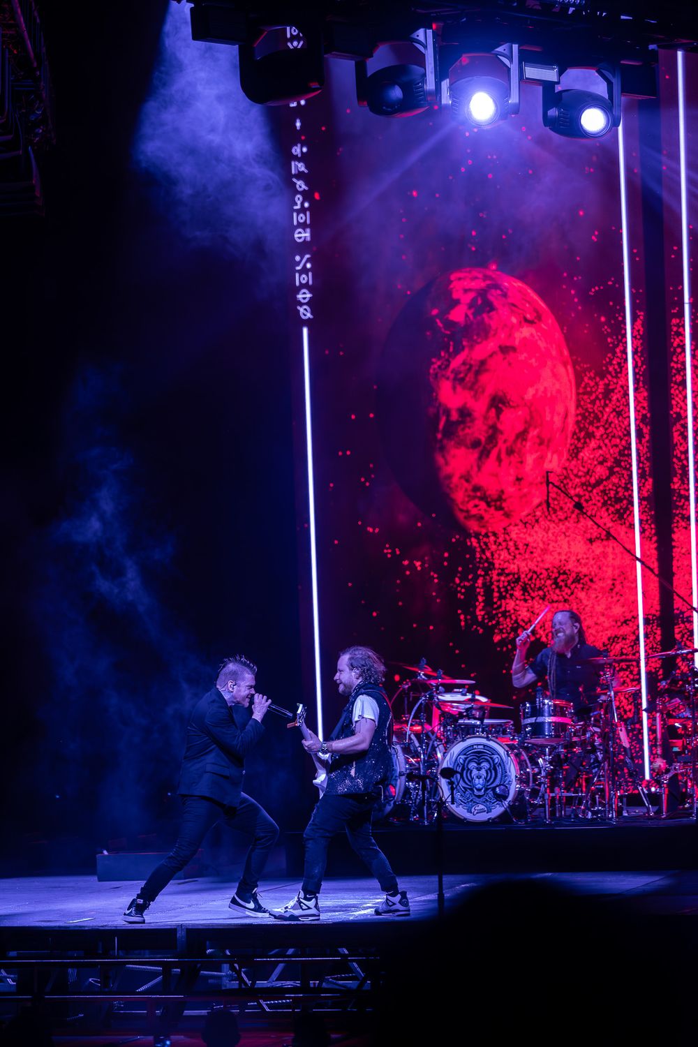 Band performs on stage with dramatic red and blue lighting and smoke effects.