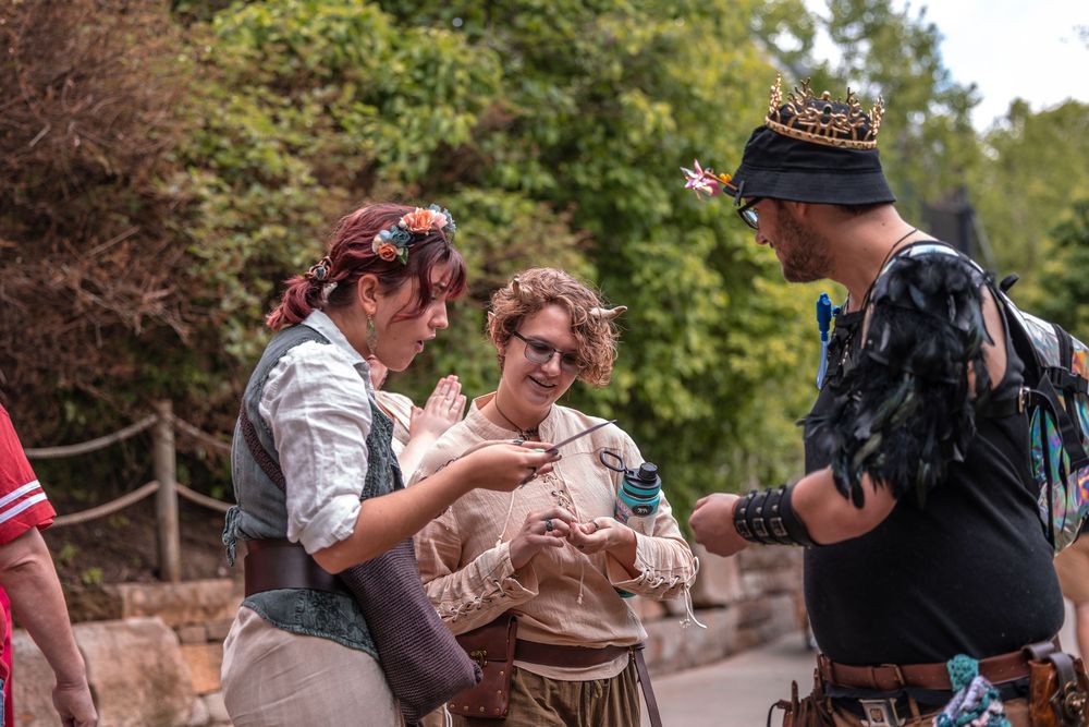 A cheerful group in period costume interacts while enjoying snacks at an outdoor renaissance faire.