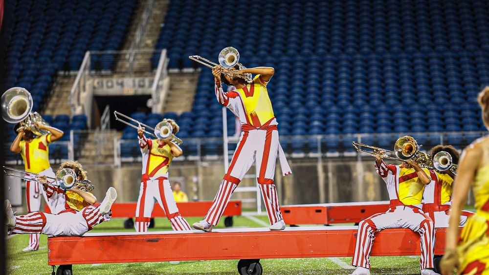 Musicians perform from elevated platforms during a marching band show at night.