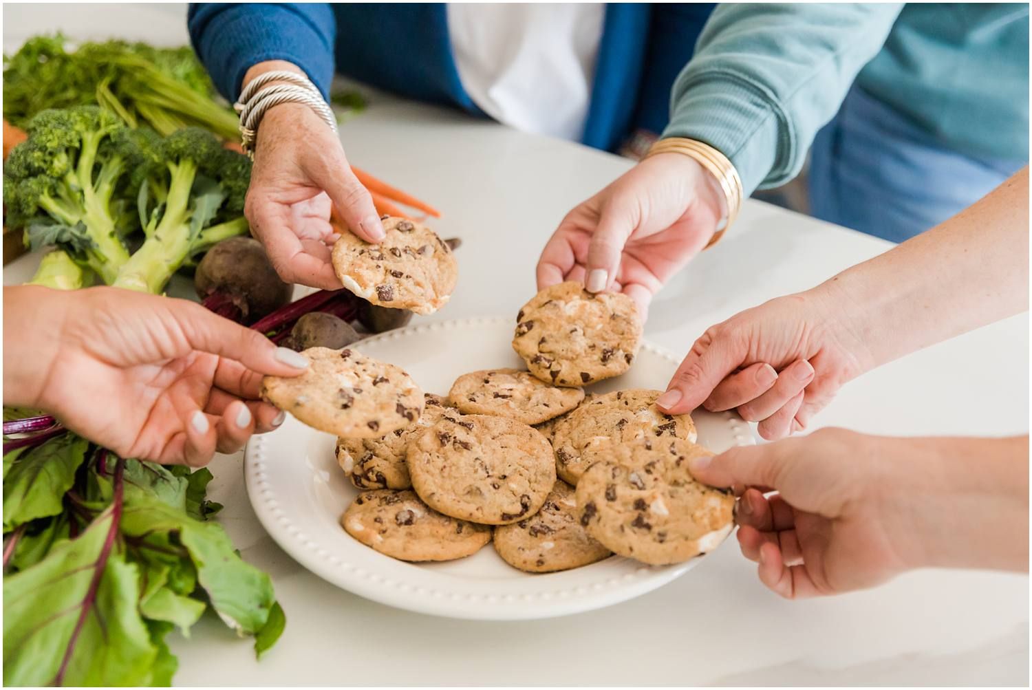 Women holding chocolate chip cookies over plate