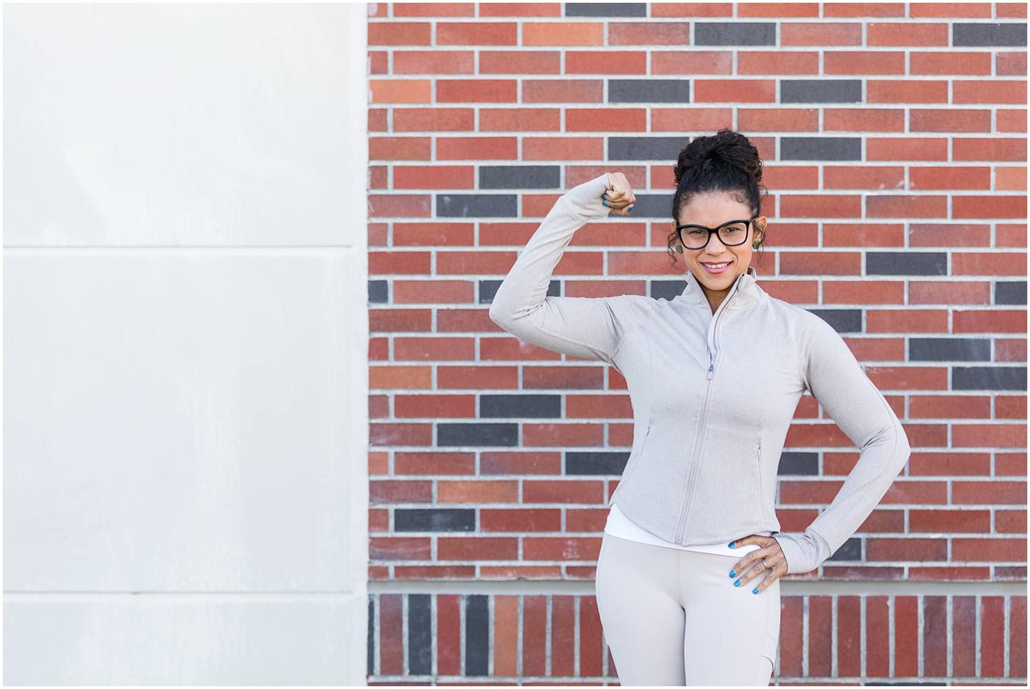 Female performing bicep pose in front of brick building
