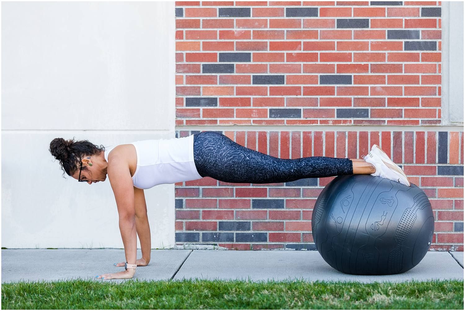 Female in plank pose with feet on fitness ball in front of brick wall