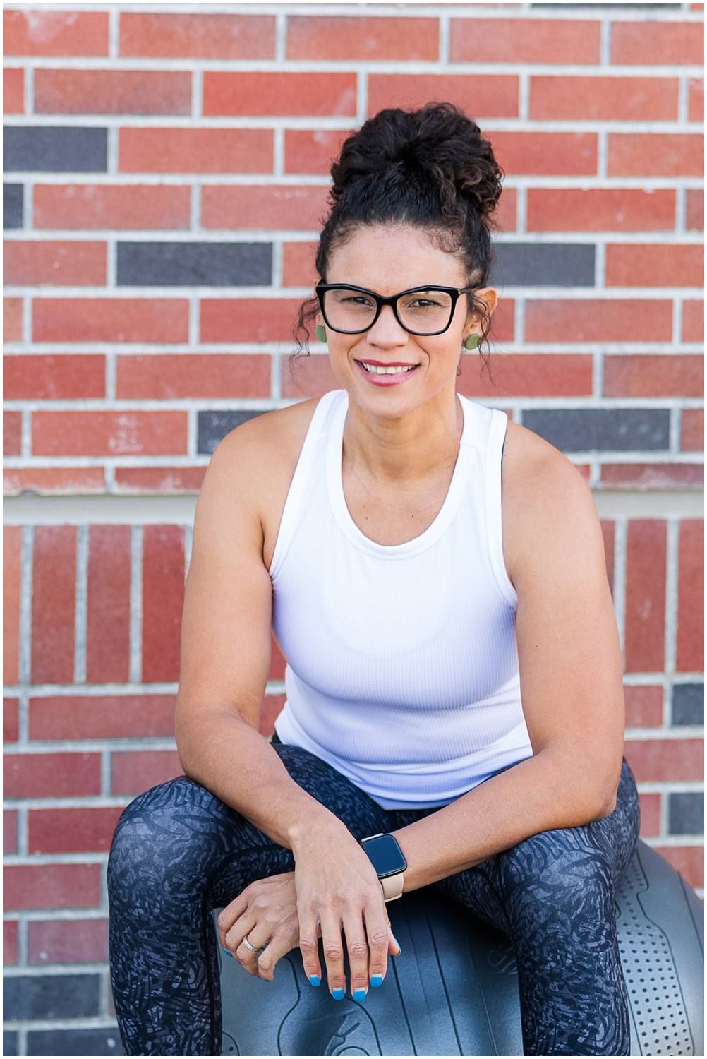 Woman posing on fitness ball in front of brick building