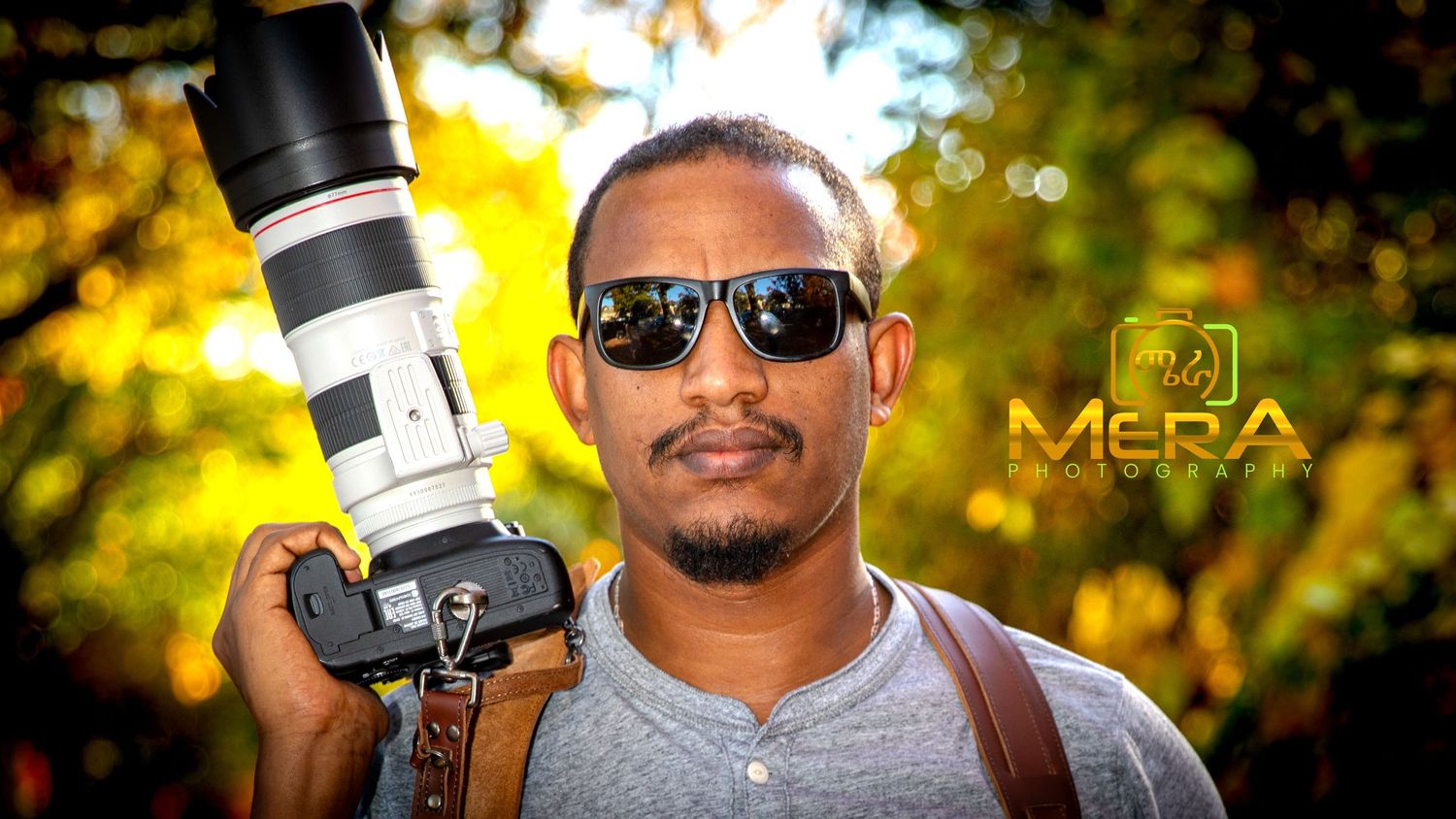 A photographer holds a professional camera with telephoto lens against golden bokeh background.
