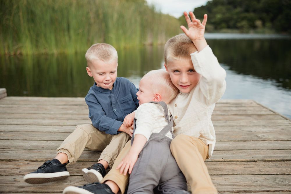 Three children share a playful moment together on a wooden dock by the water.