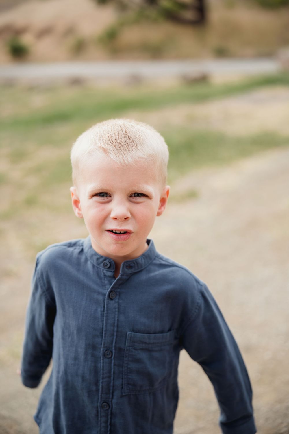A child in a navy blue shirt smiles at the camera against a natural outdoor background.