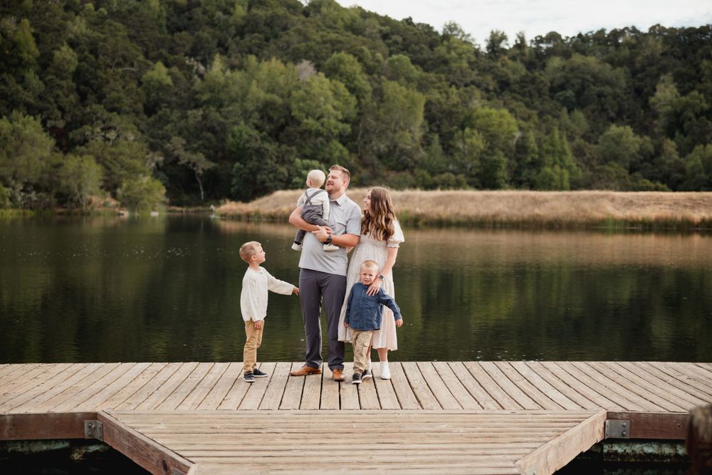 A family stands together on a wooden dock overlooking a serene lake surrounded by hills.