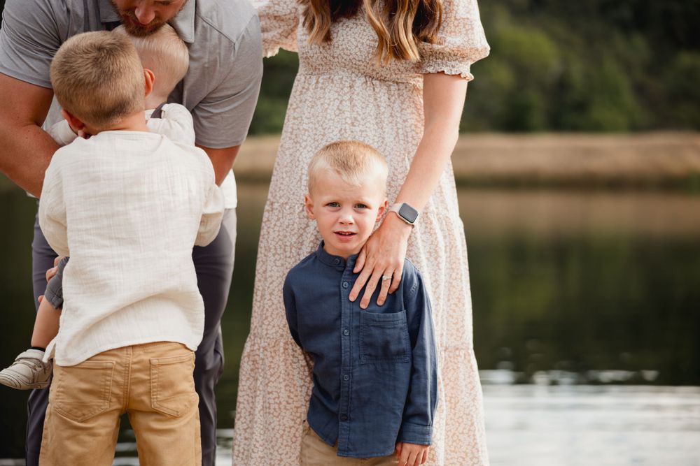 A family wearing coordinated neutral outfits poses together on a lakeside dock.