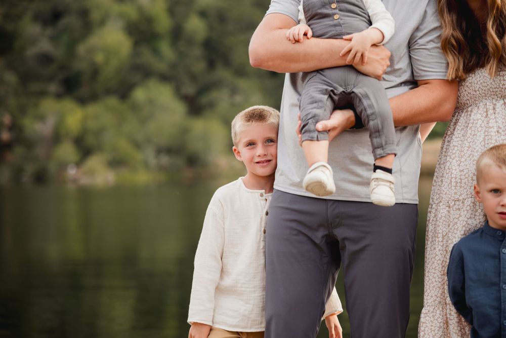 Family members in coordinating outfits stand together on a wooden dock by a peaceful lake.