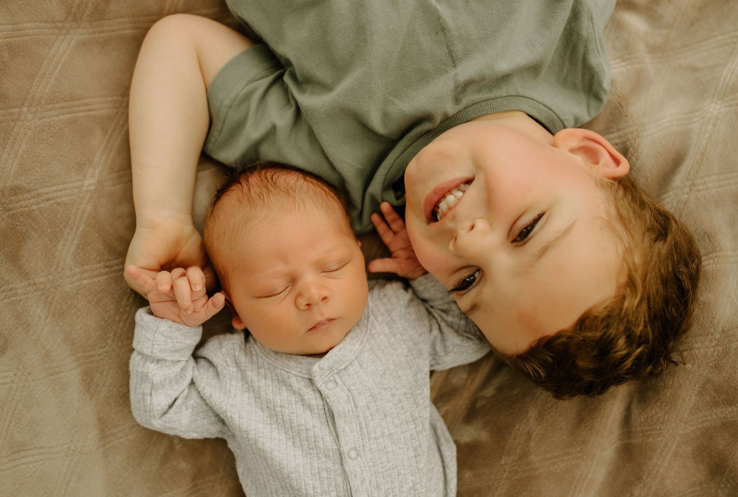 An intimate portrait of two siblings sleeping peacefully together on a beige blanket.