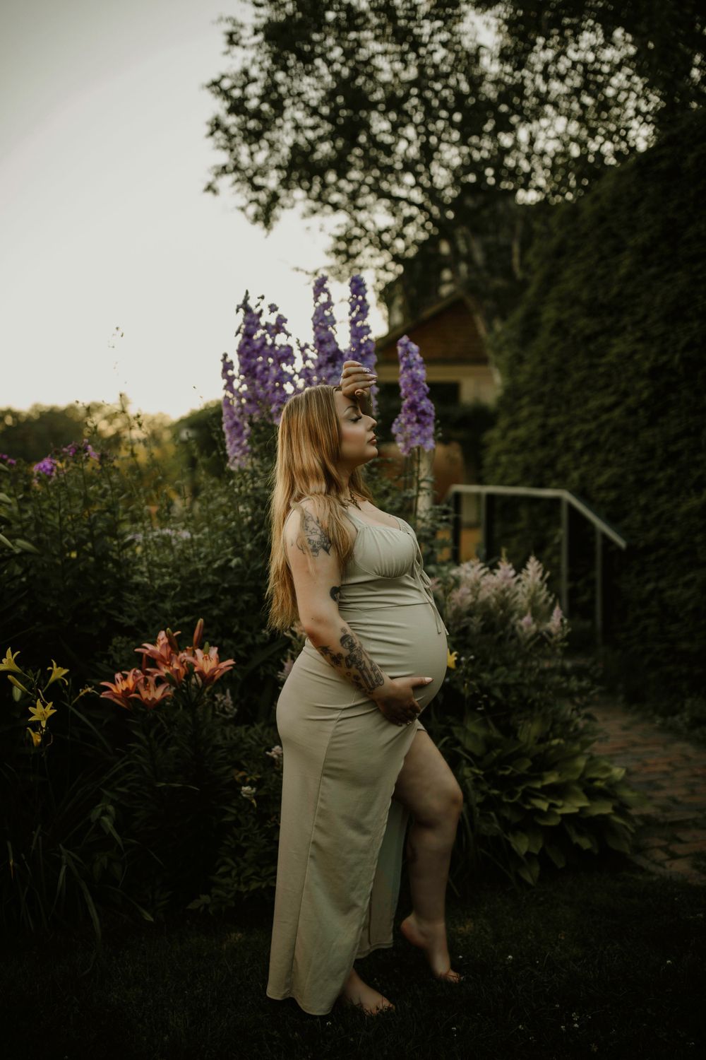Maternity portrait in a garden with blooming purple delphiniums at sunset.