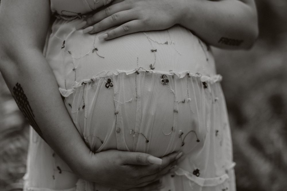 Close-up black and white photo of hands cradling a pregnant belly in a floral dress.