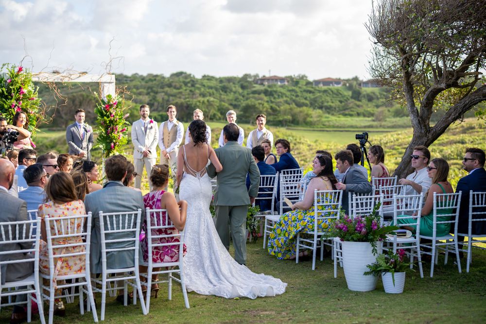 Wedding ceremony in progress with guests seated on white chairs overlooking coastal scenery.