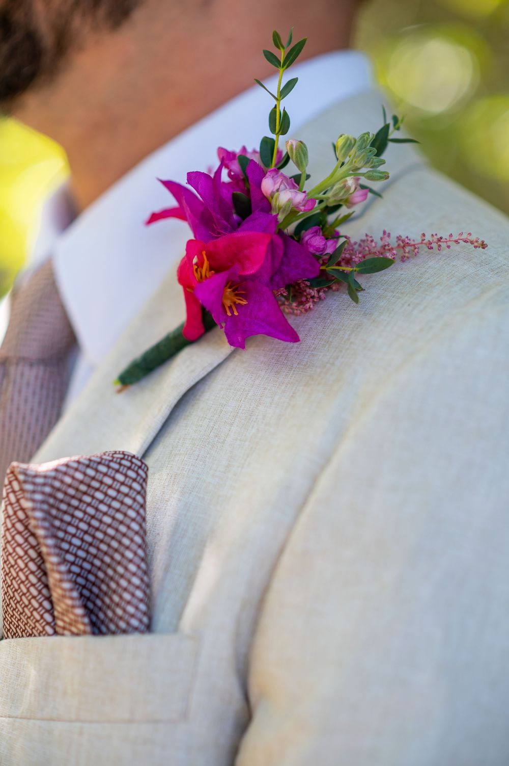 Vibrant pink floral boutonniere with greenery pinned to a light colored suit jacket.
