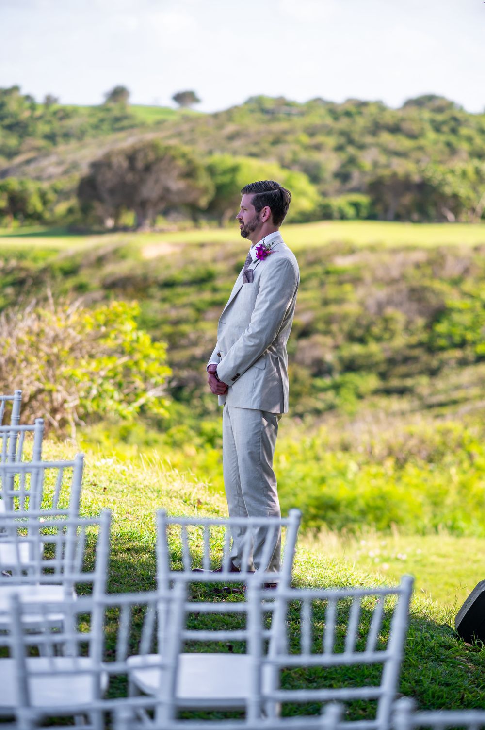 Person in grey suit standing among white chairs overlooking coastal scenery.