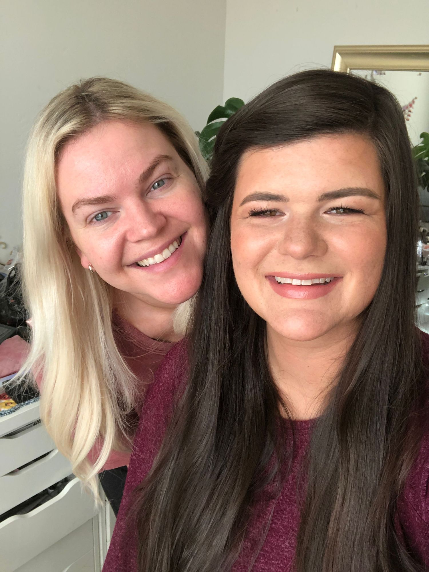 Two friends wearing matching burgundy tops smile warmly at the camera in a selfie taken indoors.