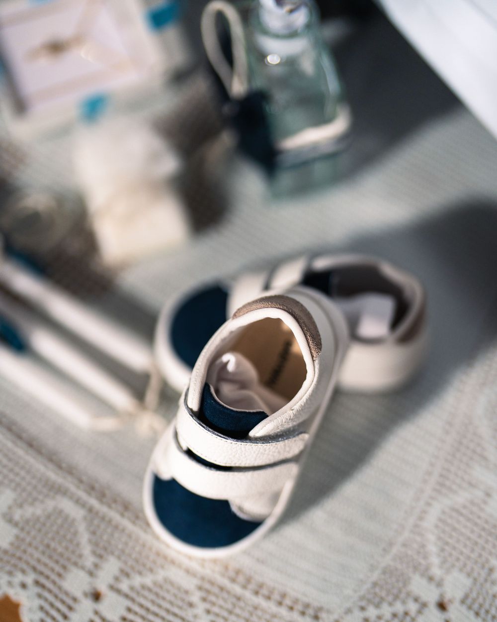 A small navy blue and white baby shoe rests on a textured white surface with blurred background elements.