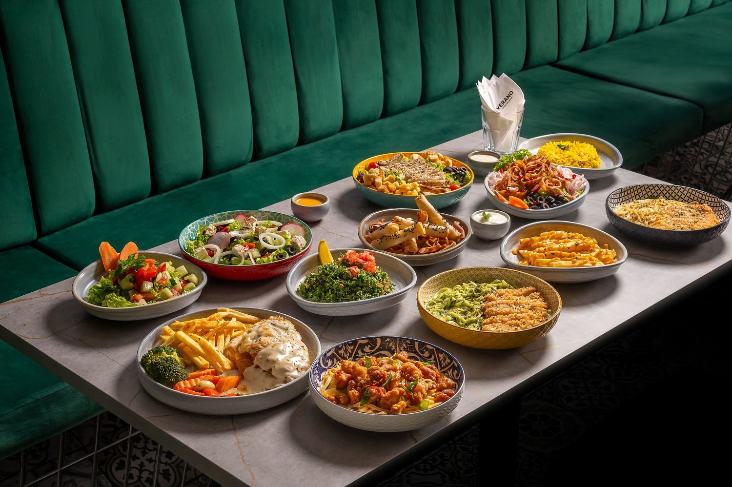 Elegant display of various international dishes arranged on white counter against green background.