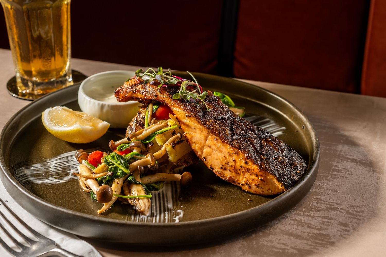 Grilled salmon fillet served with vegetables and lemon on dark plate.