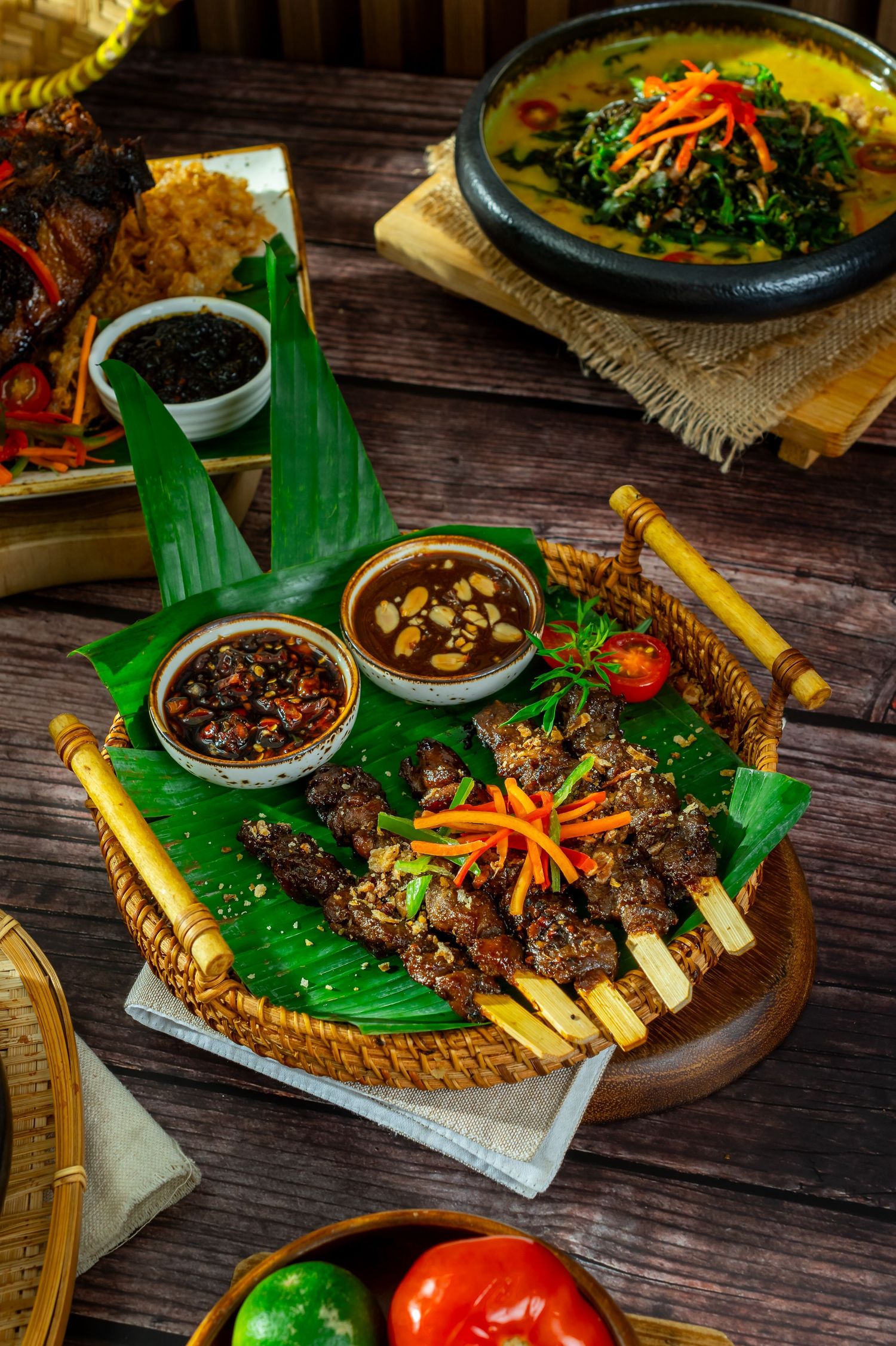 Grilled meat and seafood platter served with spices and condiments on banana leaves.