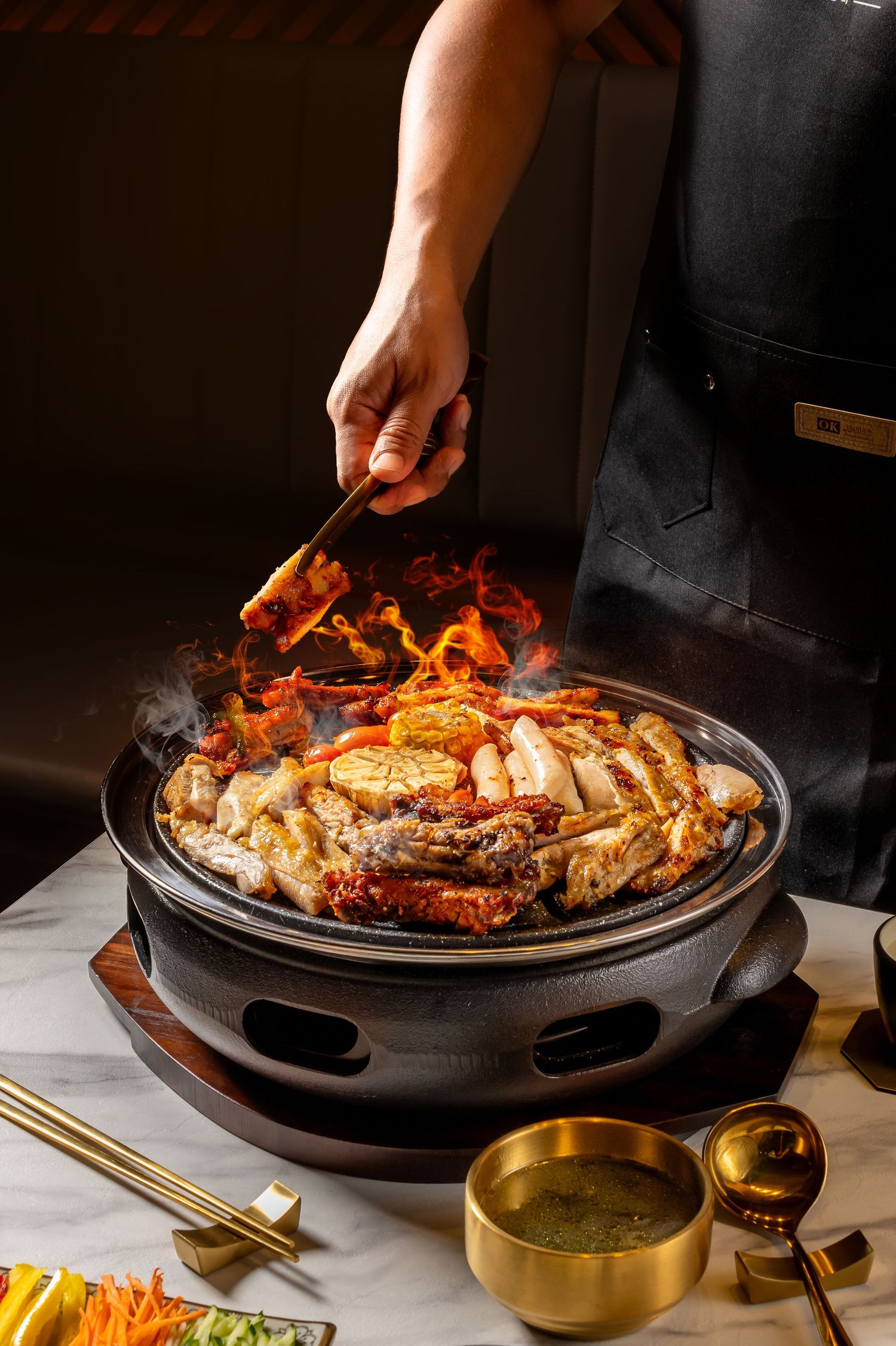Korean barbecue meats grilling on a traditional round hot plate with side dishes and chopsticks.