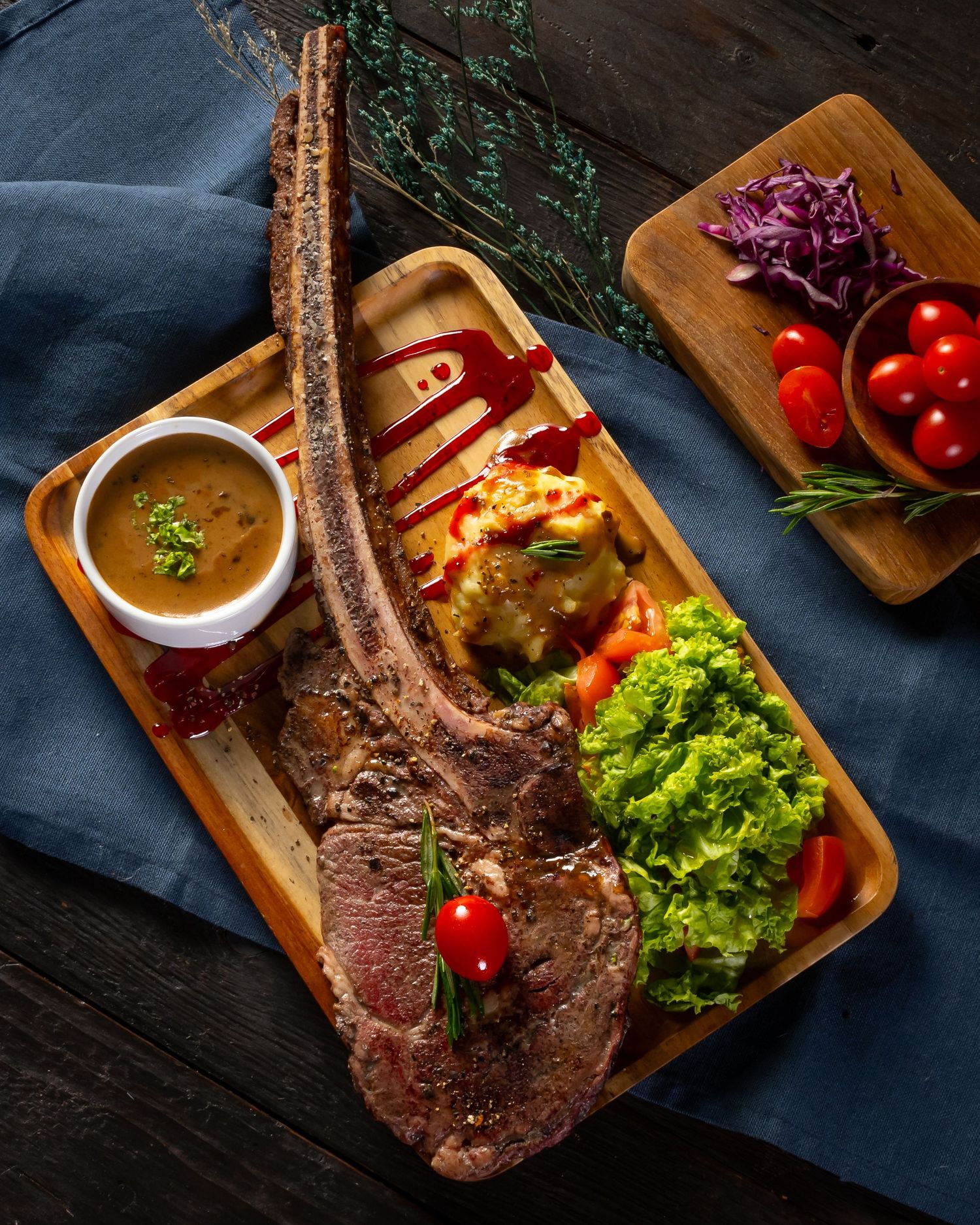 Grilled tomahawk steak served on wooden board with fresh vegetables and dipping sauce.