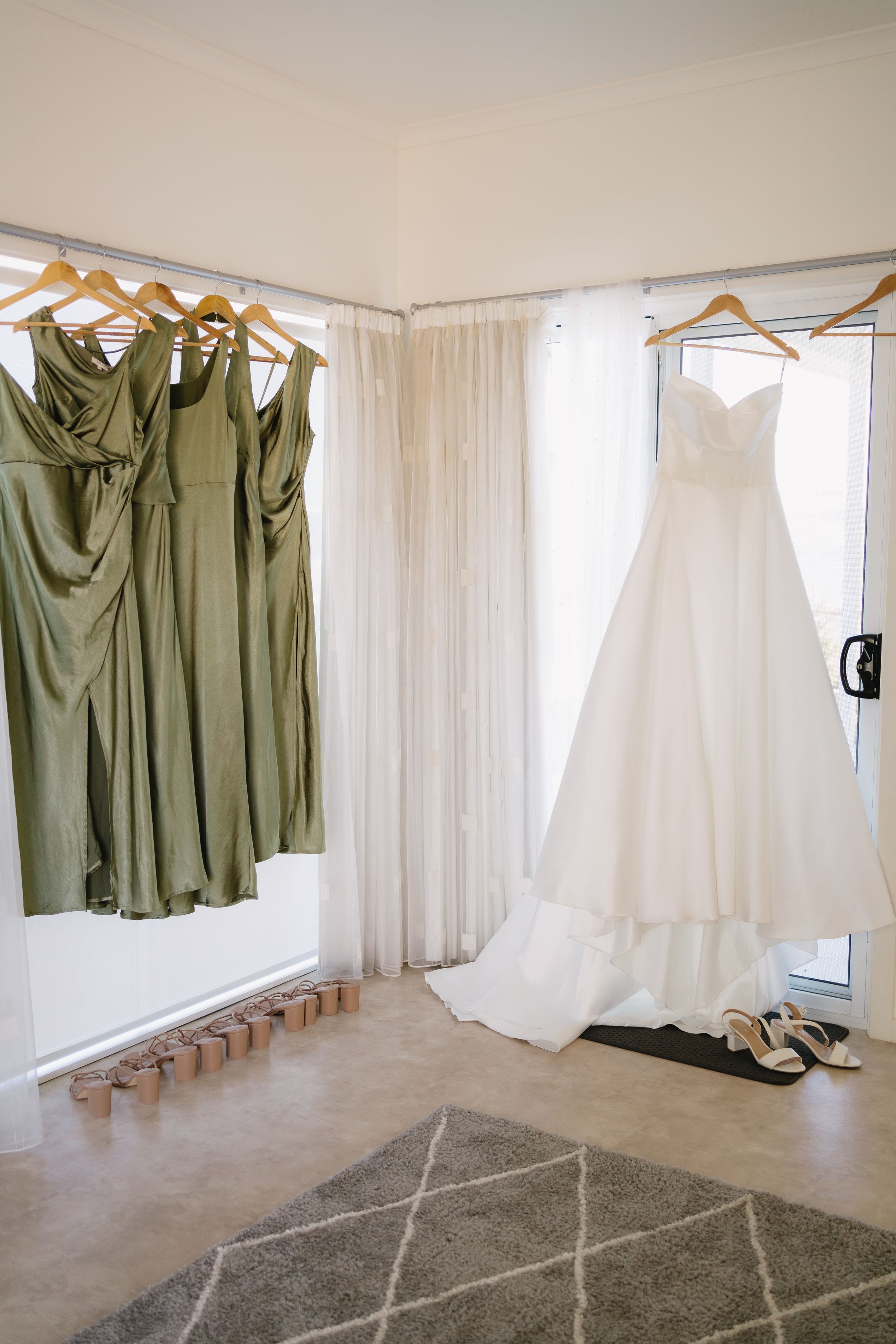 Wedding attire hanging on display with sage green bridesmaid dresses and a white bridal gown.
