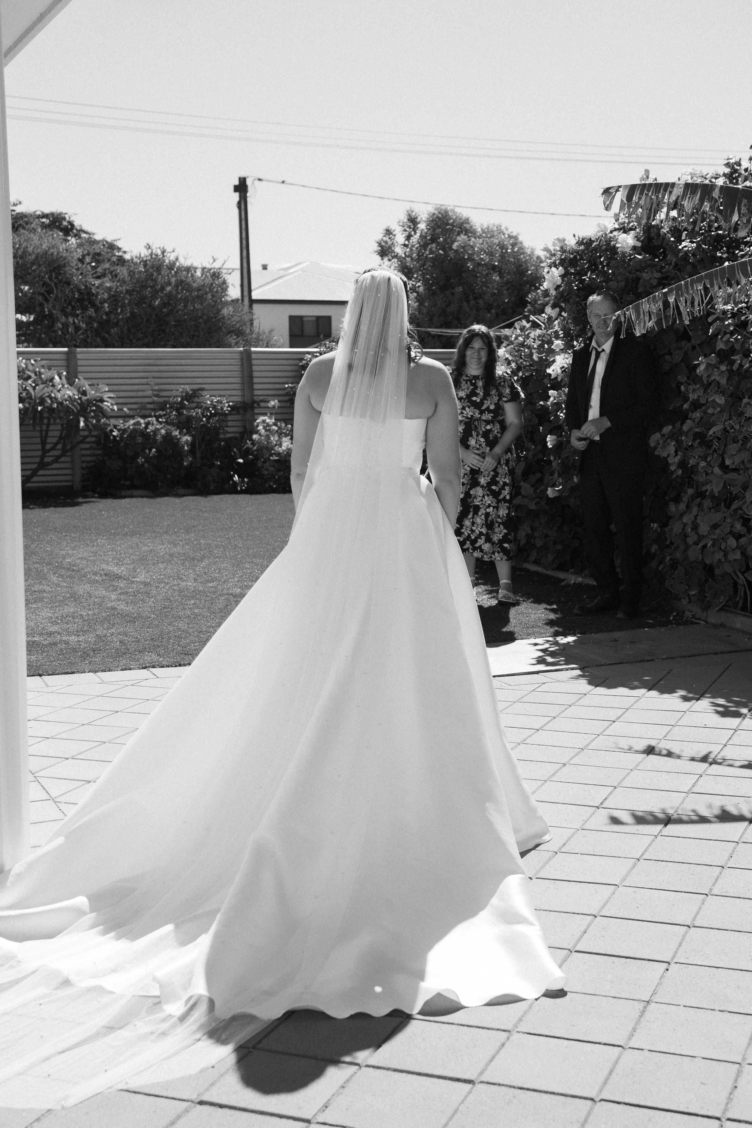 A flowing white wedding dress trails across a sunny outdoor patio.