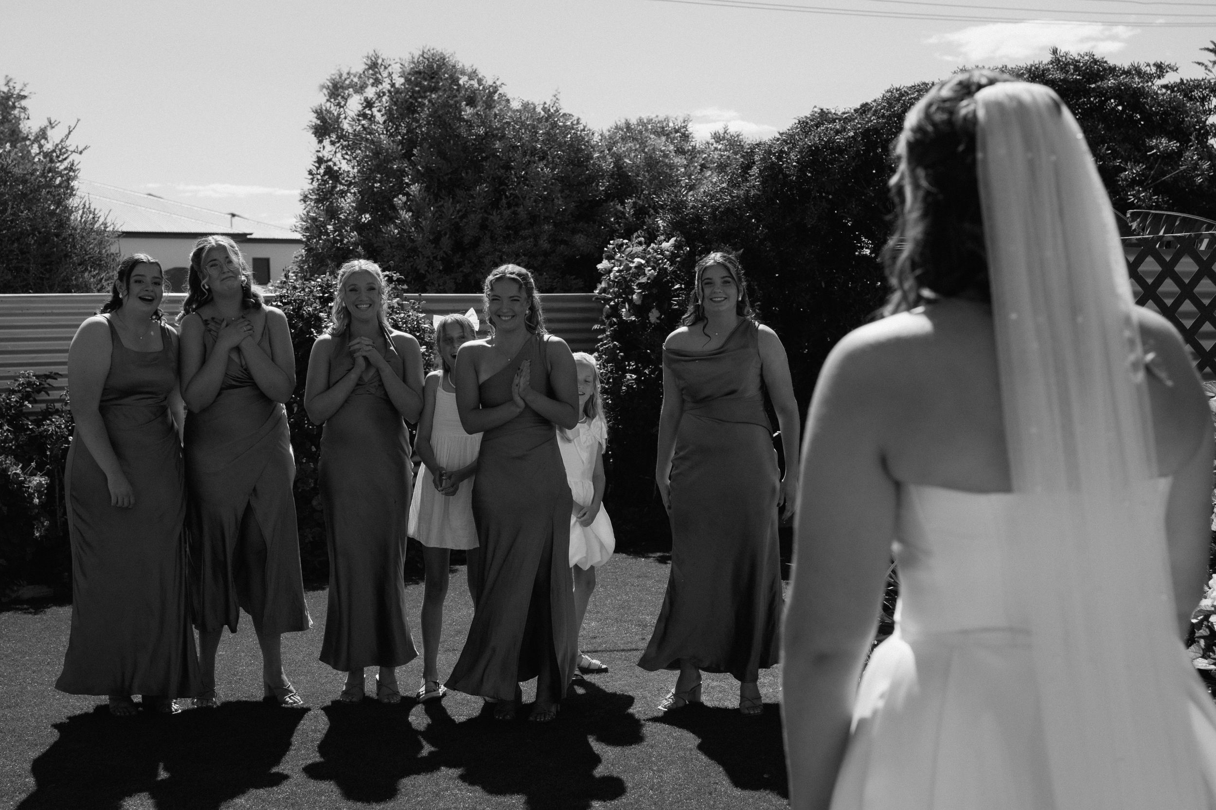 Black and white photo of bridesmaids in matching dresses laughing together outdoors at a wedding.
